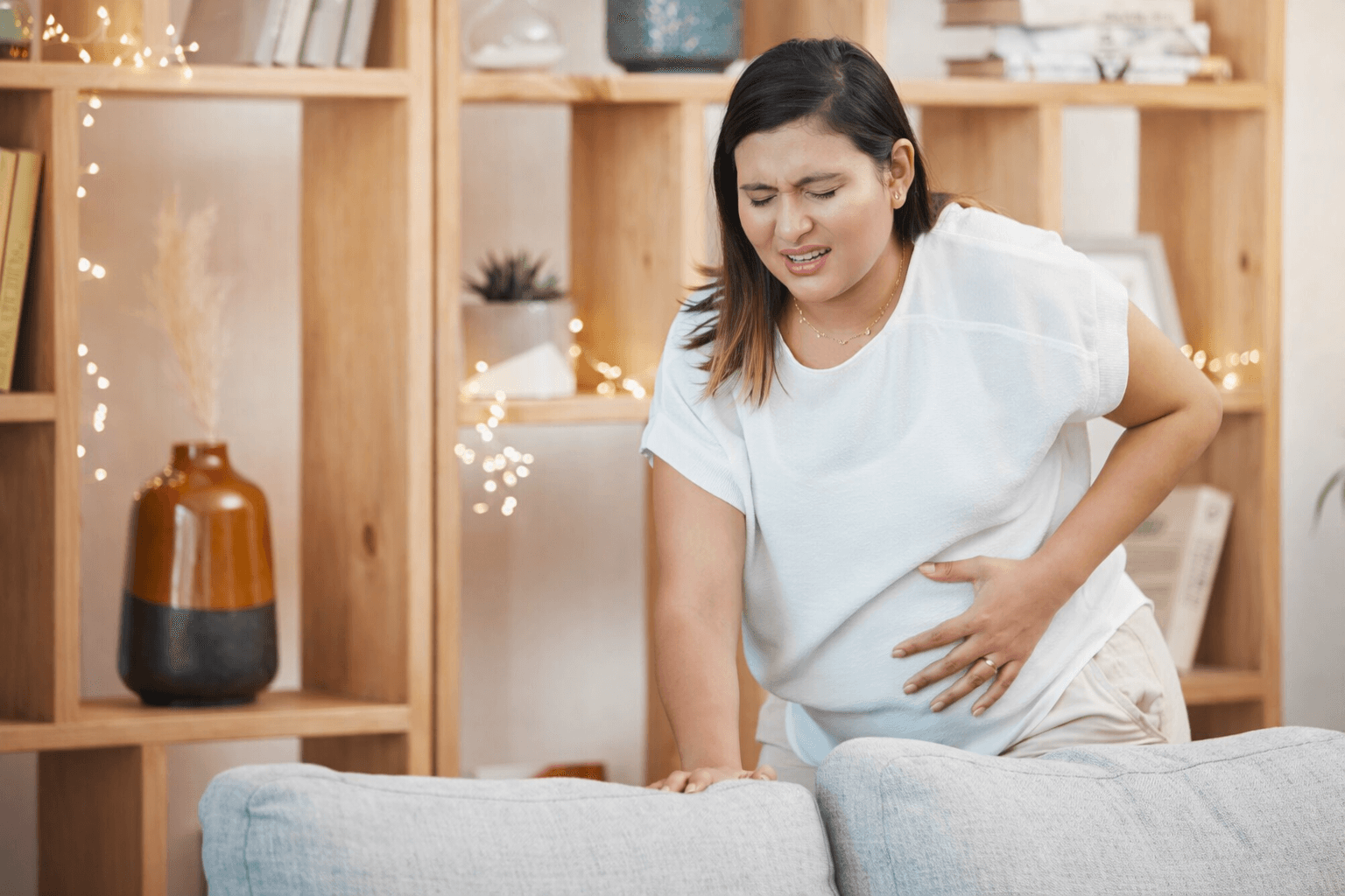 Medical Causes Of Miscarriage Woman experiencing lower abdominal pain representing medical causes of miscarriage and early pregnancy complications in a home setting