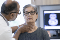 Doctor examining an older woman with visible neck swelling during an anaplastic thyroid cancer consultation