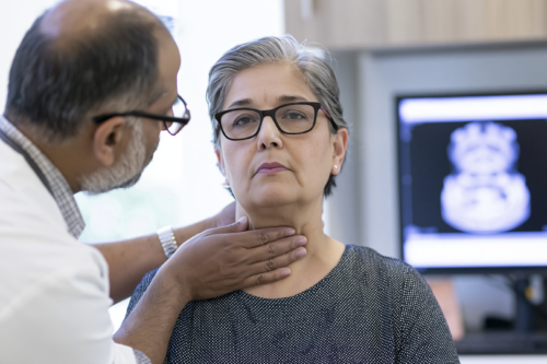 Doctor examining an older woman with visible neck swelling during an anaplastic thyroid cancer consultation