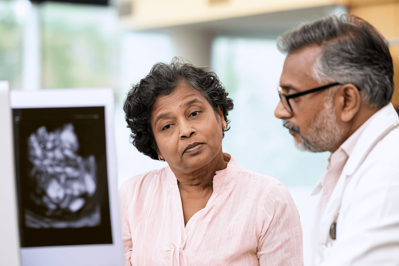 Ayurvedic doctor reviewing thyroid cancer reports with an older woman during a clinical consultation