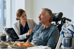 Patient with bulbar ALS receiving speech and swallowing support from a therapist using a communication tablet, with nutrition and breathing equipment.