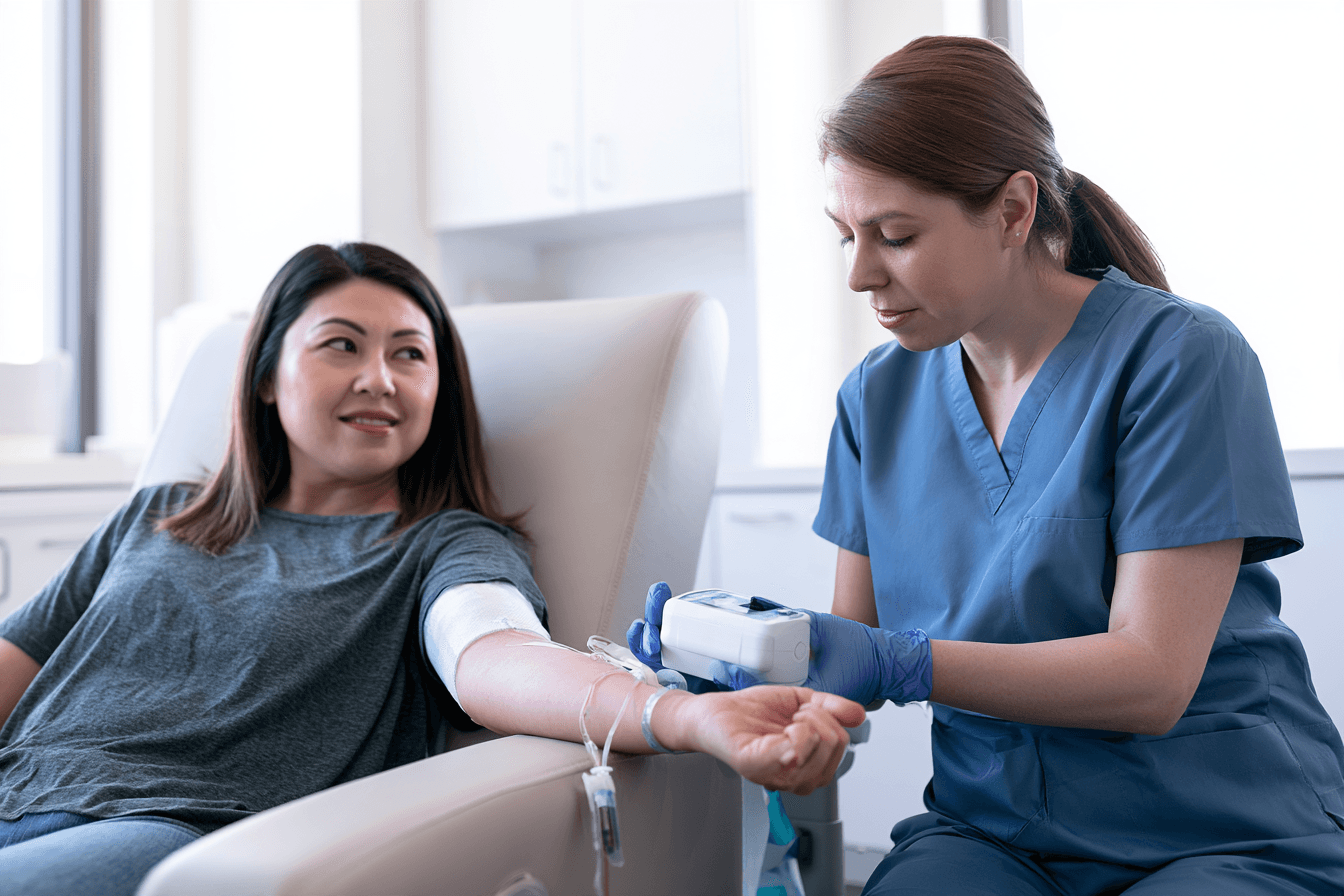 Nurse checking an infusion pump beside a patient seated in a cancer treatment recliner.