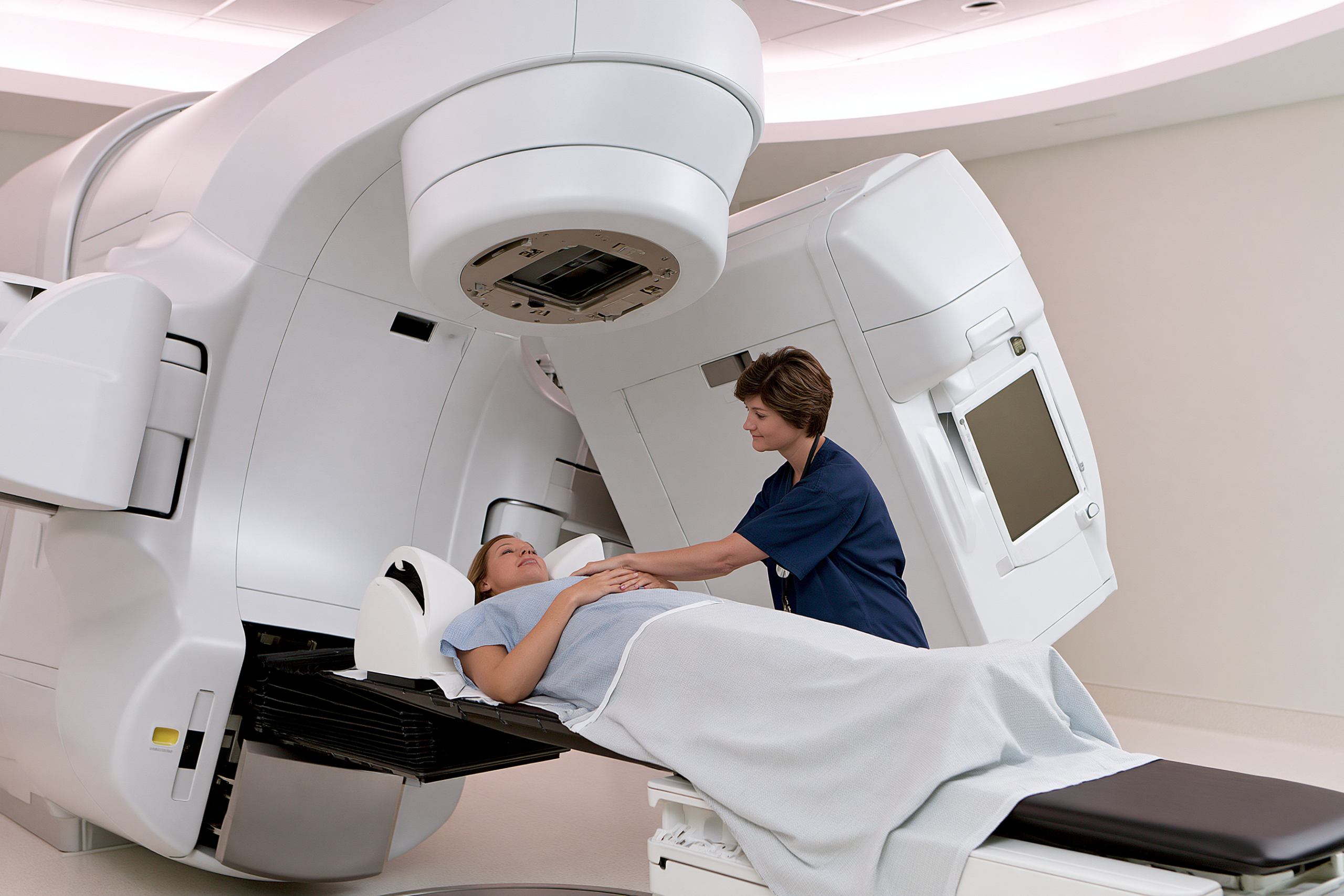 Radiation therapist positioning a patient on a treatment couch beneath a linear accelerator.