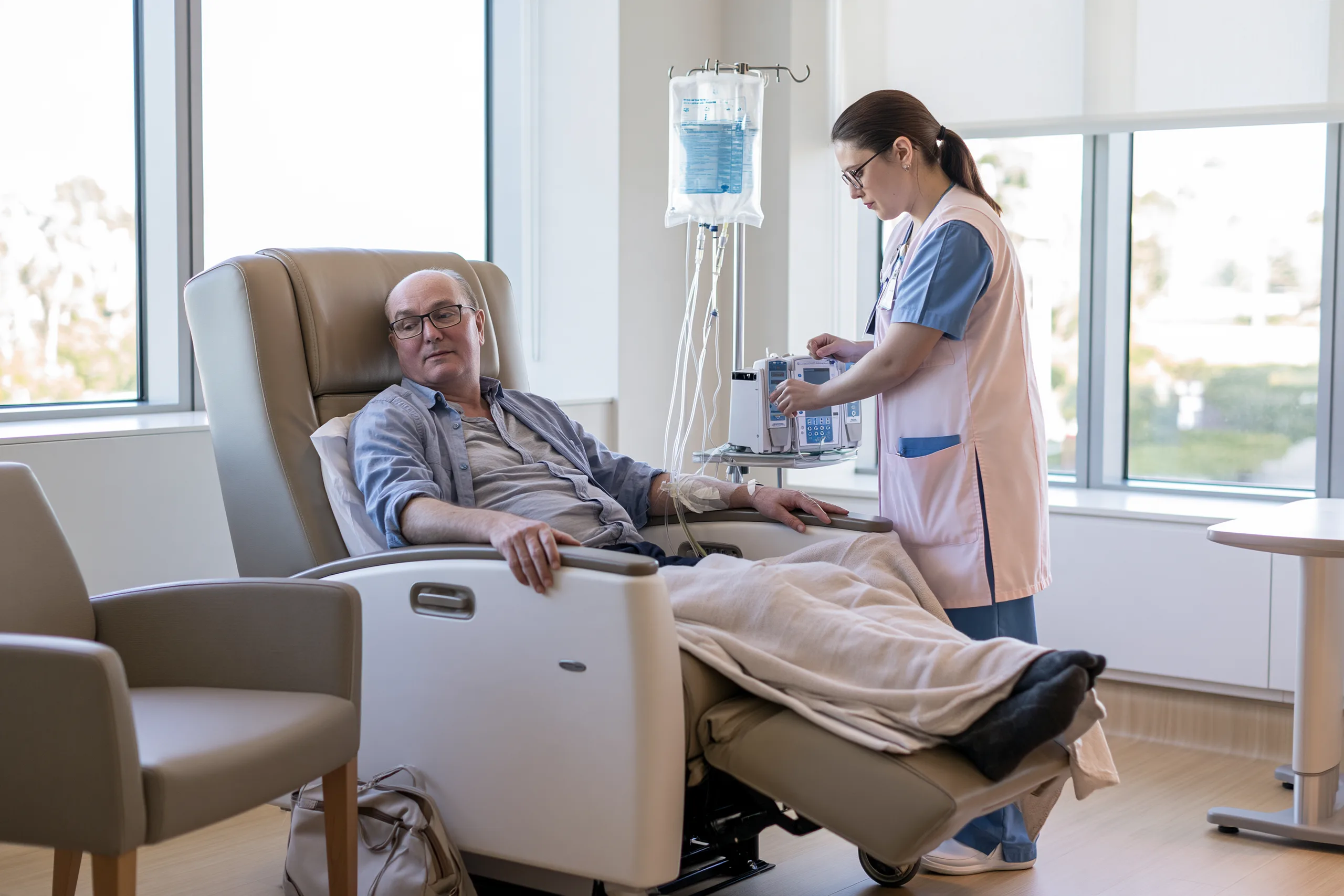Metastatic Esophageal Cancer Treatment: Biomarker-Guided Care 2 Oncology nurse checking an infusion pump beside a patient seated in a modern treatment recliner.