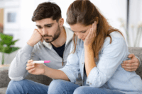 Couple looking worried at pregnancy test representing infertility causes diagnosis treatment for couples trying to conceive.