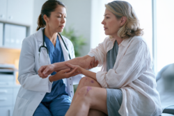 Doctor examining petechiae and unexplained bruising on a patient’s arm and leg during leukemia evaluation.