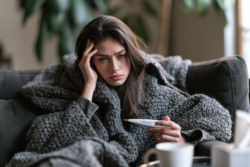 Young woman checking a thermometer while feeling tired, showing possible leukemia symptoms such as fever, fatigue, and early illness signs.
