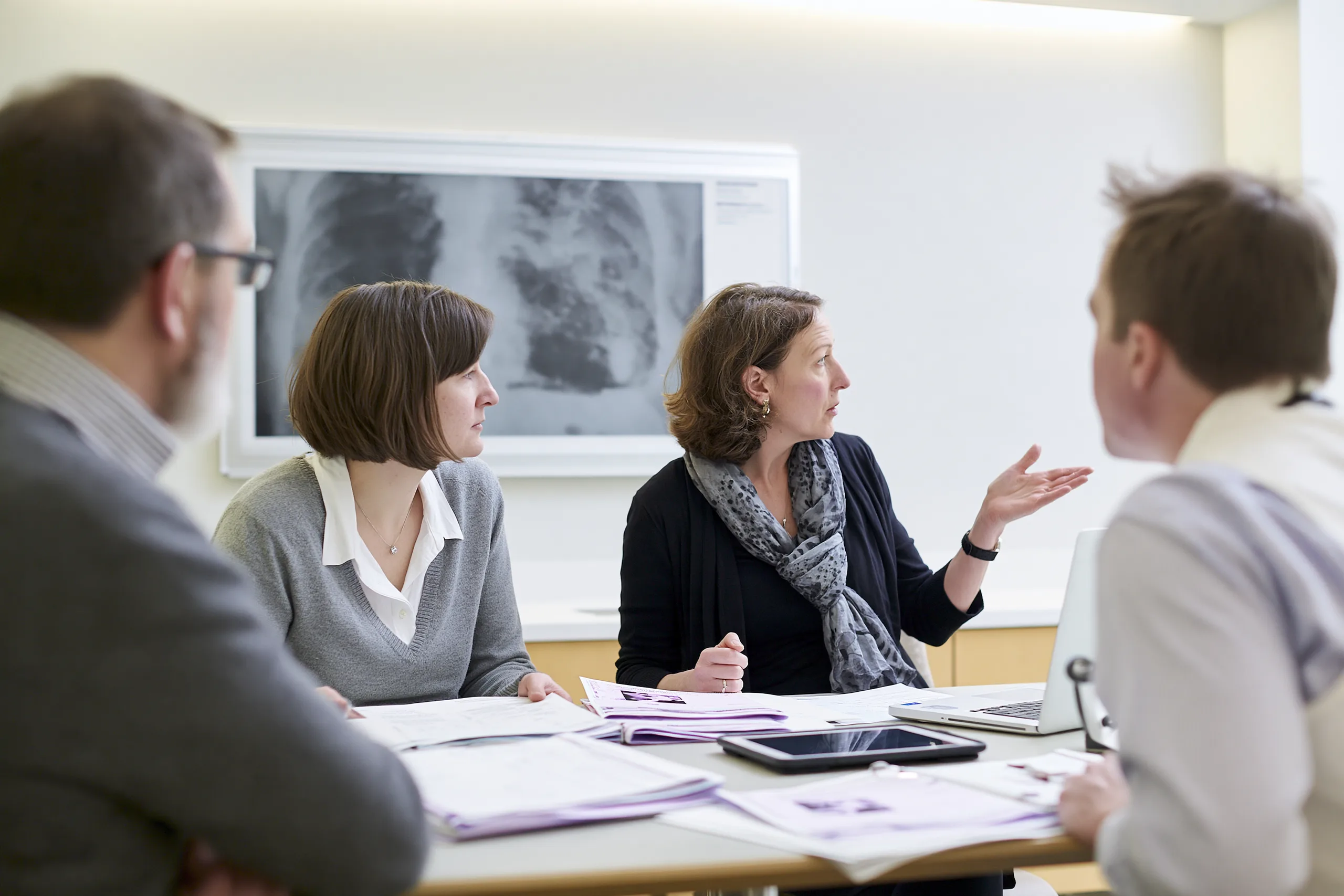 Metastatic Esophageal Cancer Treatment: Biomarker-Guided Care 5 Three clinicians discussing medical reports and chest imaging during a multidisciplinary case review.